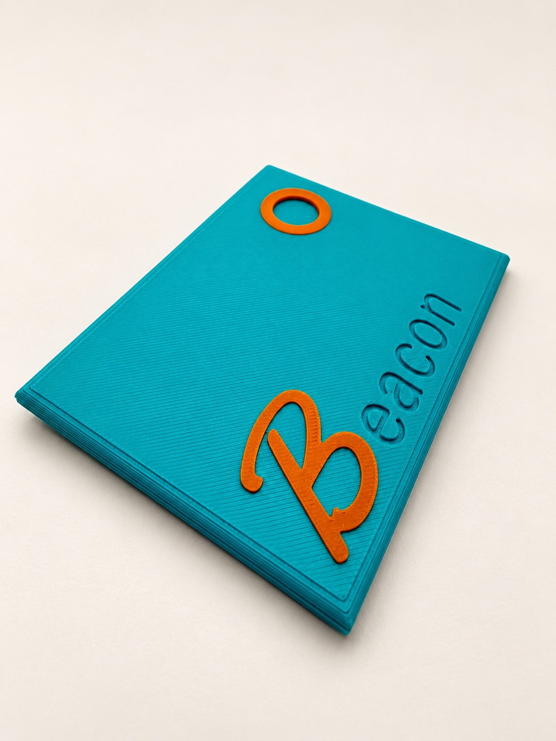 Teal Binder Beacon tracker with an orange B and circular accent, photographed at an angle